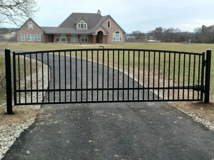Automated arched wrought iron driveway gate in front of a brick ranch home