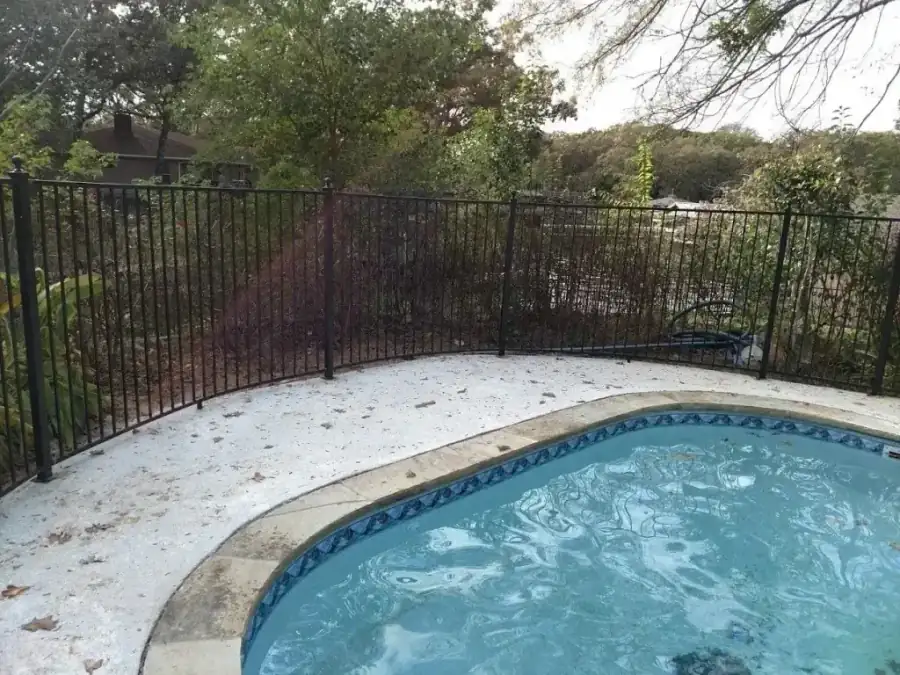 Black ornamental iron fence curving around a pool deck