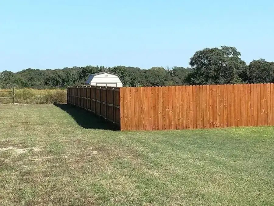 A long run of freshly stained dog-ear cedar privacy fence crossing a pasture in Athens, Texas